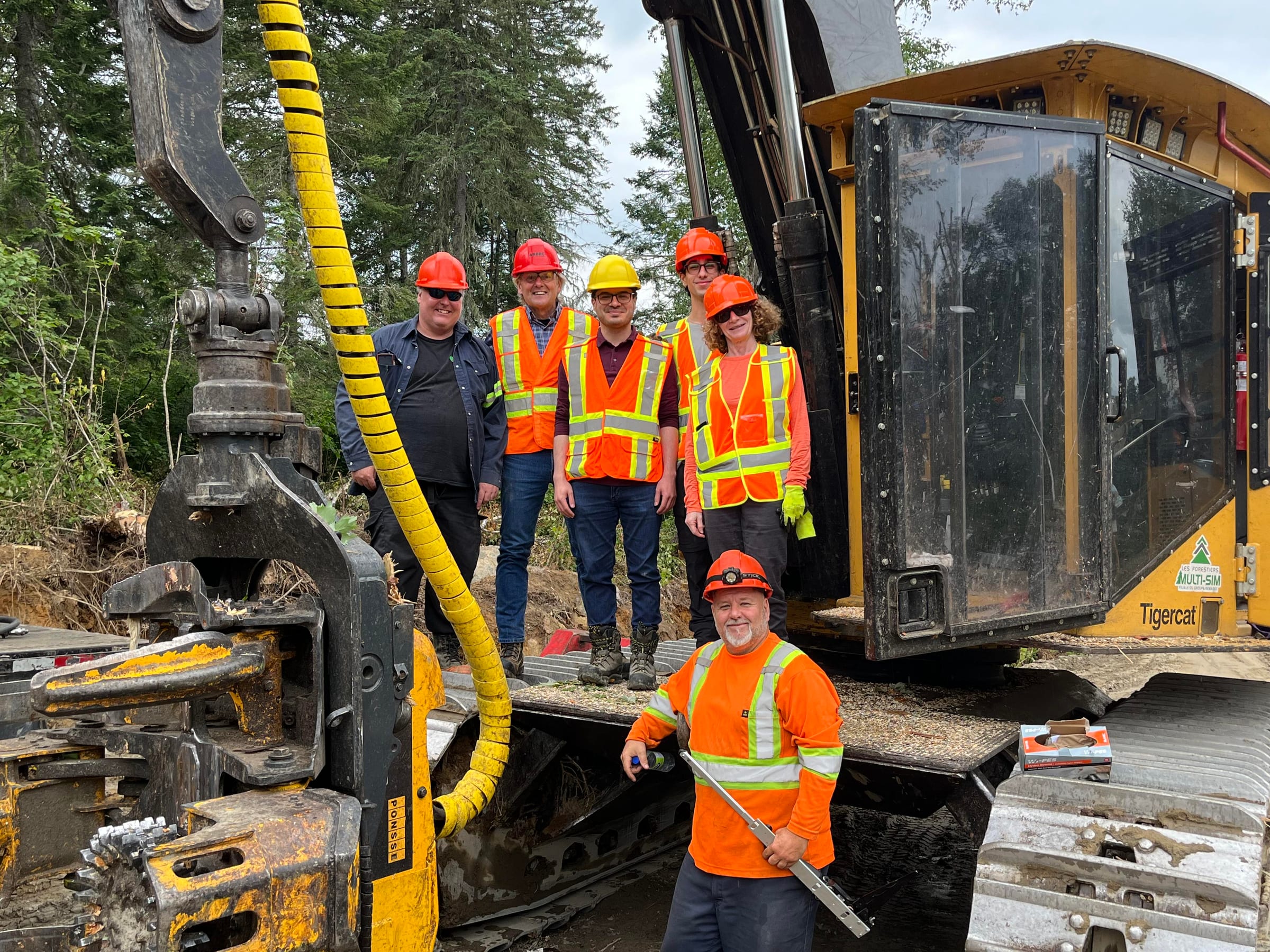 The team and forestry crew in hard hats and safety vests on a Tigercat machine at a field pilot